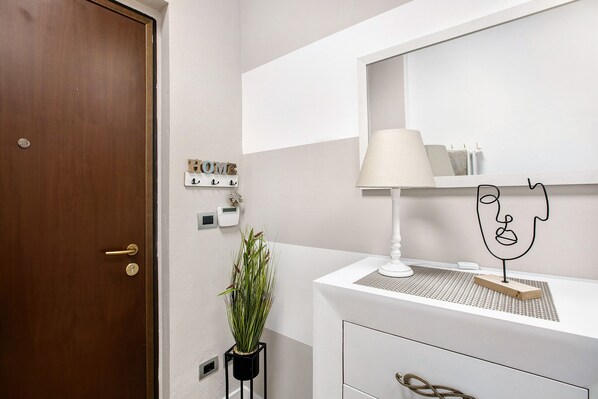 A bathroom with a wooden door, a white vanity, a mirror, a lamp, a plant, and a wall-mounted light switch. - Studio Apartment "Little House Aosta" with Wi-Fi (Aosta)