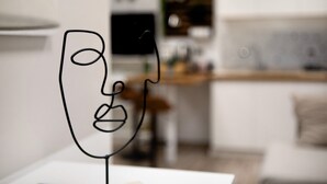 Una habitación minimalista con una mesa blanca, una silla negra y un fondo desenfocado que sugiere una sala de estar.