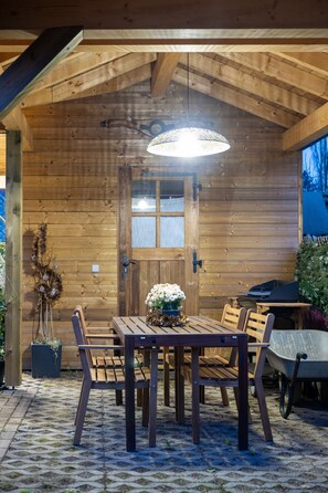 A wooden cabin with a dining table and chairs, a wheelbarrow, and a hanging light fixture. - Holiday Apartment "Gite Béthanie" with Mountain View, Private Wooden Terrace & Wi-Fi (Steige)