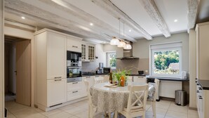 A modern kitchen with white cabinetry, a dining table with chairs, and a window with a view of greenery. - Holiday Apartment "Gite Béthanie" with Mountain View, Private Wooden Terrace & Wi-Fi (Steige)