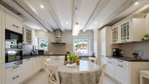 A modern kitchen with white cabinets, a dining table with a leaf-patterned tablecloth, and a view of a house through a window. - Holiday Apartment "Gite Béthanie" with Mountain View, Private Wooden Terrace & Wi-Fi (Steige)