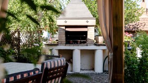 An outdoor brick oven barbecue area with a table and chairs in the foreground. - Holiday Apartment "Gite Béthanie" with Mountain View, Private Wooden Terrace & Wi-Fi (Steige)