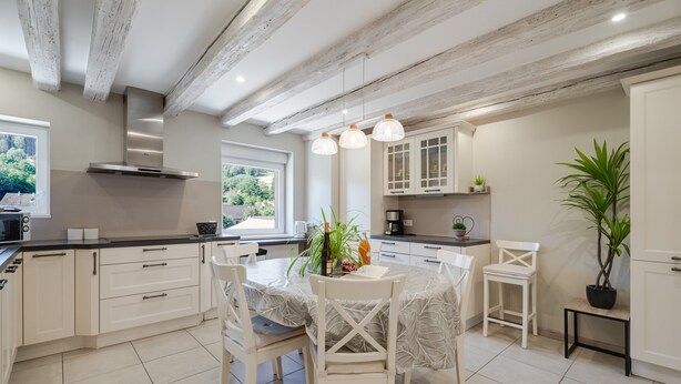 A modern kitchen with white cabinetry, a dining table with chairs, and a view of greenery outside. - Holiday Apartment "Gite Béthanie" with Mountain View, Private Wooden Terrace & Wi-Fi (Steige)
