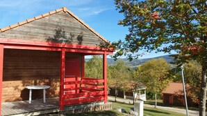 Een houten chalet met een rode deur en een klein terras, omgeven door bomen en uitzicht op een berg.