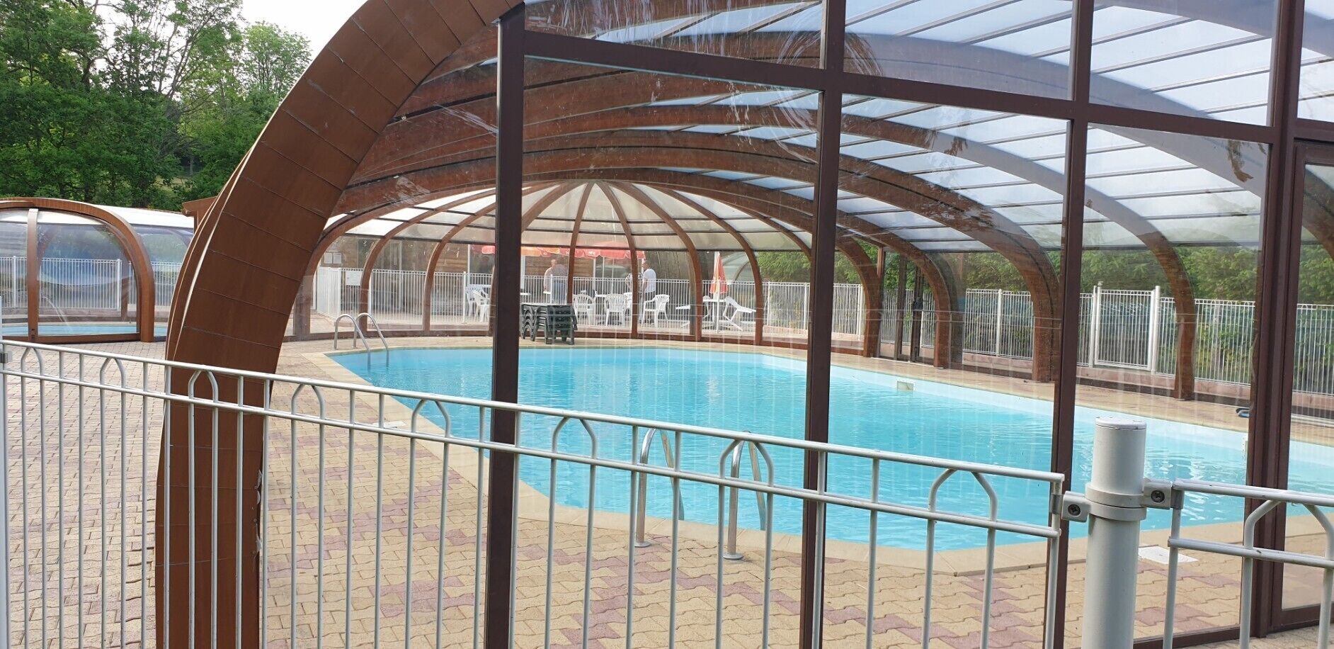 Una piscina techada con barandilla metálica, rodeada por un patio de ladrillo.