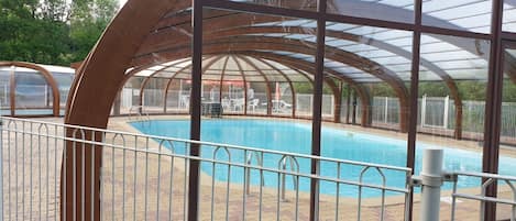 Una piscina techada con barandilla metálica, rodeada por un patio de ladrillo.