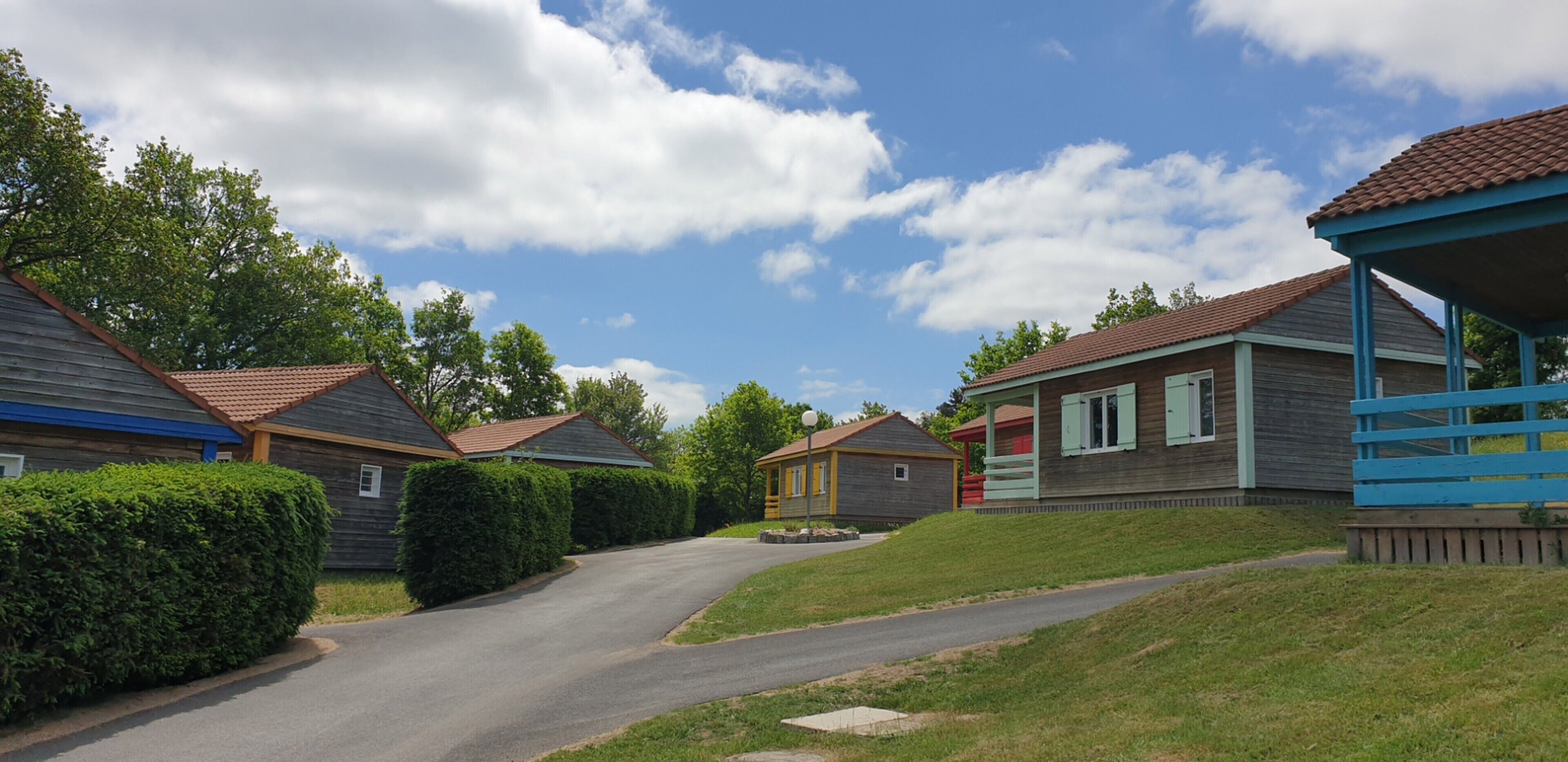 A row of wooden cabins with a paved driveway and a grassy area.