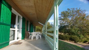 A covered porch with a wooden floor, white plastic chairs, and a green fence. - Chalet Aster 1 with Mountain View, Shared Pool and Wi-Fi (BLAVIGNAC)