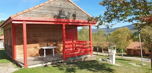 A wooden cabin with a red porch, a small table, and a view of mountains.