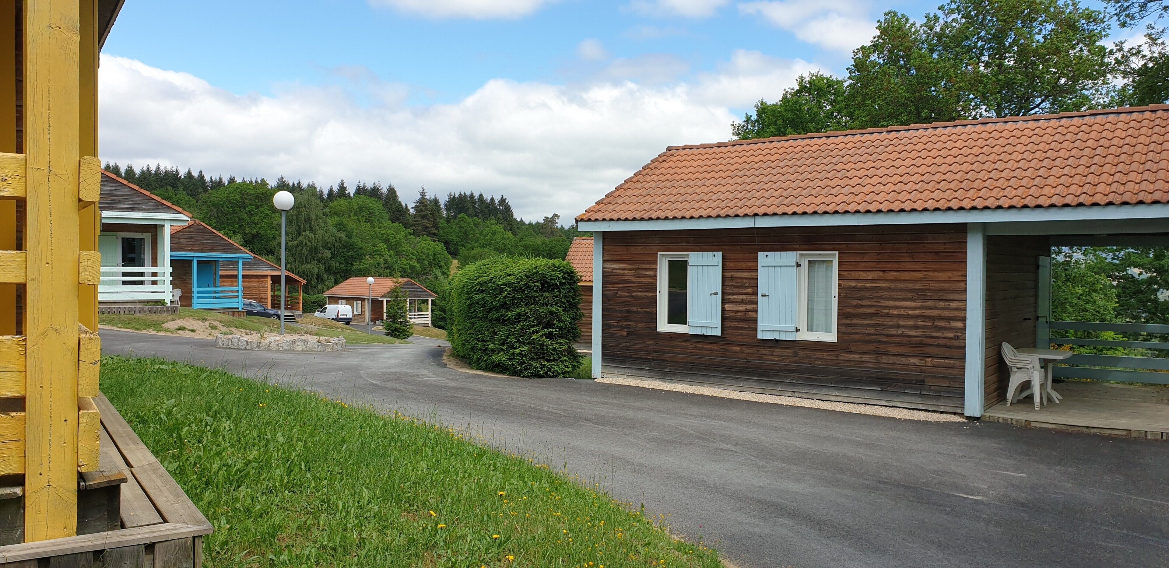 A row of wooden cabins with a paved road in front, surrounded by greenery.