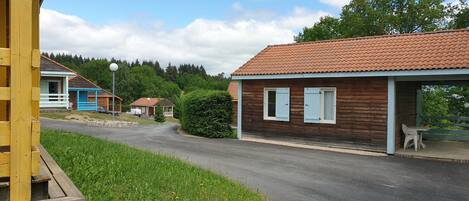 A row of wooden cabins with a paved road in front, surrounded by greenery.