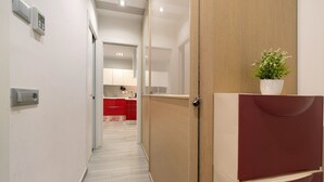 Un pasillo con una puerta de madera, una planta en maceta y una cocina roja al fondo.