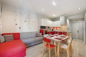 Eine moderne Wohnung mit Essbereich, Küchenzeile und Wohnraum mit Sofa und rotem Akzent.