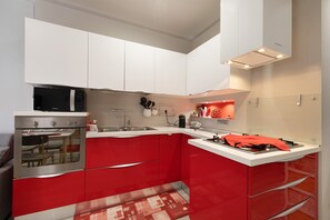 Eine moderne Küche mit weißen Oberschränken, einem roten Unterschrank, Edelstahlgeräten und einer roten Spritzschutzwand.