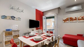 Un comedor con una mesa dispuesta para cuatro personas, un sofá rojo y un televisor montado en la pared.