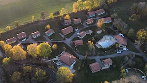 An aerial view of a residential area with multiple houses, a large open field, and a circular structure. - Chalet 'Hibiscus for 6, Weekend Price' with Mountain View, Shared Pool, and Wi-Fi (Blavignac)