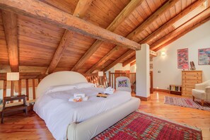 Ein Schlafzimmer mit Holzbalkendecke, einem großen Bett, einem Sessel, einem Schminktisch und einem Teppich.