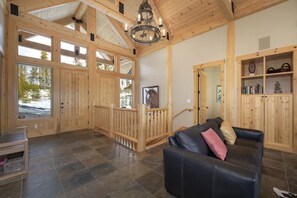 A spacious room with a black leather sofa, wooden walls, and a large window.