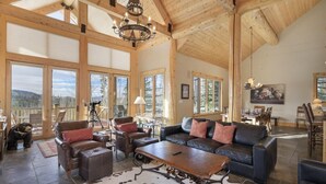 A spacious living room with large windows, a chandelier, leather furniture, and a cowhide rug.