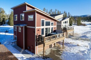 A two-story house with a deck, large windows, and a snowy landscape.