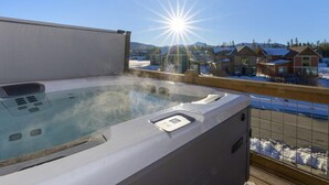 Ett bubbelbad med en kontrollpanel, omgivet av ett trädäck, med utsikt över ett bostadsområde med hus och ett snötäckt landskap.