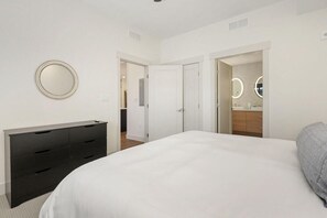 A bedroom with a bed, a dresser, a mirror, and a bathroom with a sink and mirror.