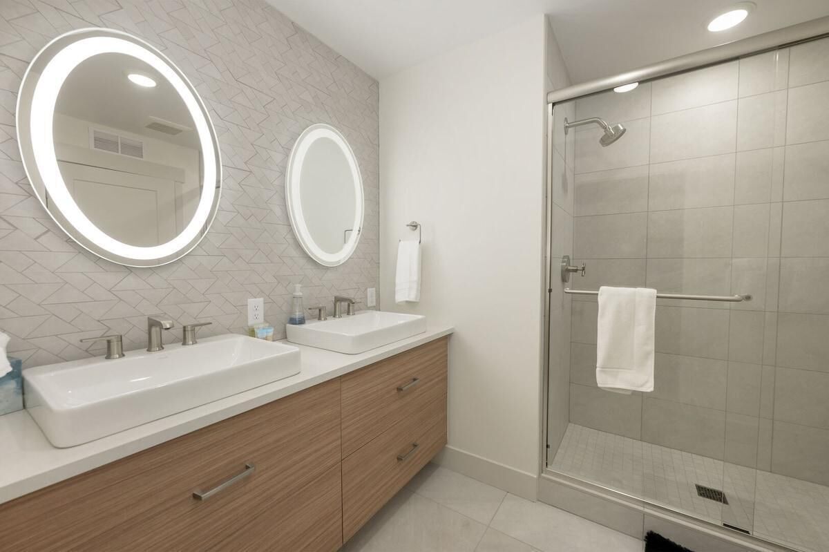 A modern bathroom with two sinks, a large mirror, and a glass shower enclosure.