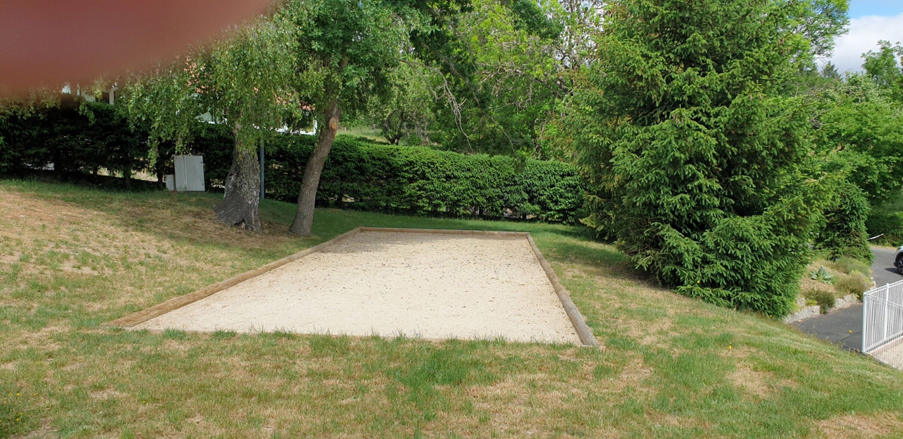 A backyard with a sandpit, a tree, and a hedge.