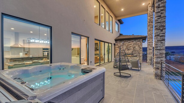 A modern outdoor hot tub area with a stone wall and glass doors leading to a kitchen. - Scenic Sunvilla Monthly Home| Private Pool, Hot Tub, Basketball Court (Hurricane)