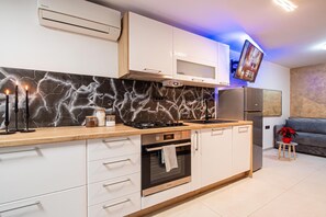 A modern kitchen with white cabinetry, a black marble backsplash, a built-in oven, and a stainless steel refrigerator.