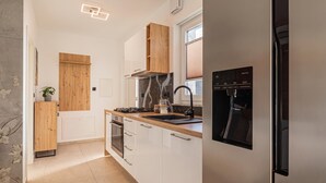 Une cuisine moderne avec des armoires blanches, une porte en bois, un four encastré, une cuisinière en acier inoxydable et un réfrigérateur noir.