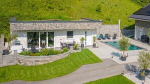 Une maison moderne dotée d’une piscine, d’un patio avec des sièges et d’une pelouse bien entretenue.