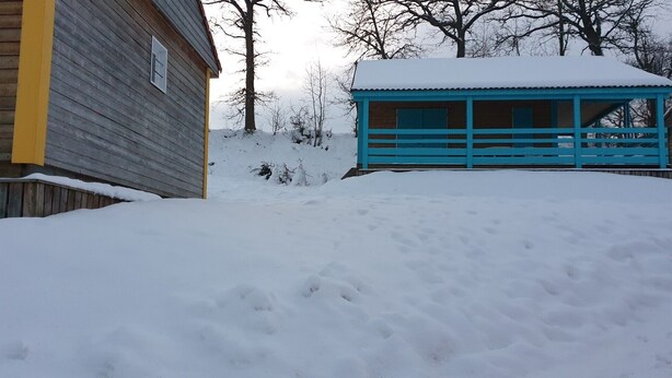 Eine verschneite Außenlandschaft mit einem Holzbauten und einer blauen Struktur.