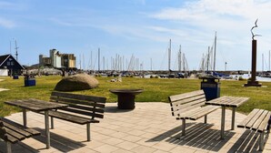 A waterfront park with benches, a large rock, and a marina in the background.