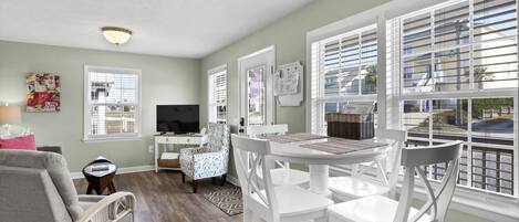 A living room with a dining area, a television, and a window with blinds.