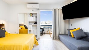 A modern hotel room with a bed, a sofa, a TV, a bookshelf, and a balcony with a view. - Beautiful Studio in front of the sea in Costa Adeje (Adeje)