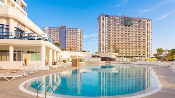 A hotel pool area with lounge chairs, a pool, and high-rise buildings in the background. - Beautiful Studio in front of the sea in Costa Adeje (Adeje)