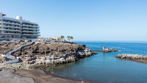 A coastal hotel with a rocky shoreline, clear blue sea, and a paved walkway leading to the beach. - Beautiful Studio in front of the sea in Costa Adeje (Adeje)