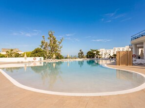 Une piscine avec des chaises longues, une clôture en bois et une vue sur un immeuble doté de balcons.
