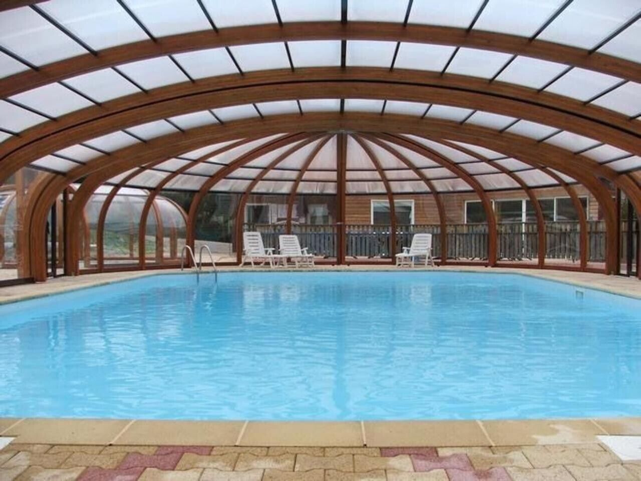 An indoor swimming pool with a wooden arched roof and white lounge chairs.