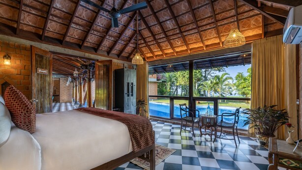 A spacious bedroom with a large bed, checkered floor, and a view of a swimming pool. - Amã Stays & Trails Lily Pad , Kumarakom (Kottayam)