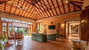 A spacious living area with a high ceiling, brick walls, and a large window providing natural light. - Amã Stays & Trails Lily Pad , Kumarakom (Kottayam)