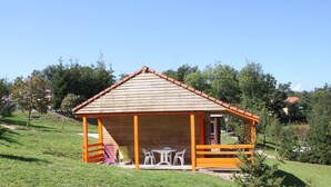 Een houten hut met een puntige kap, een veranda met stoelen en een tafel.