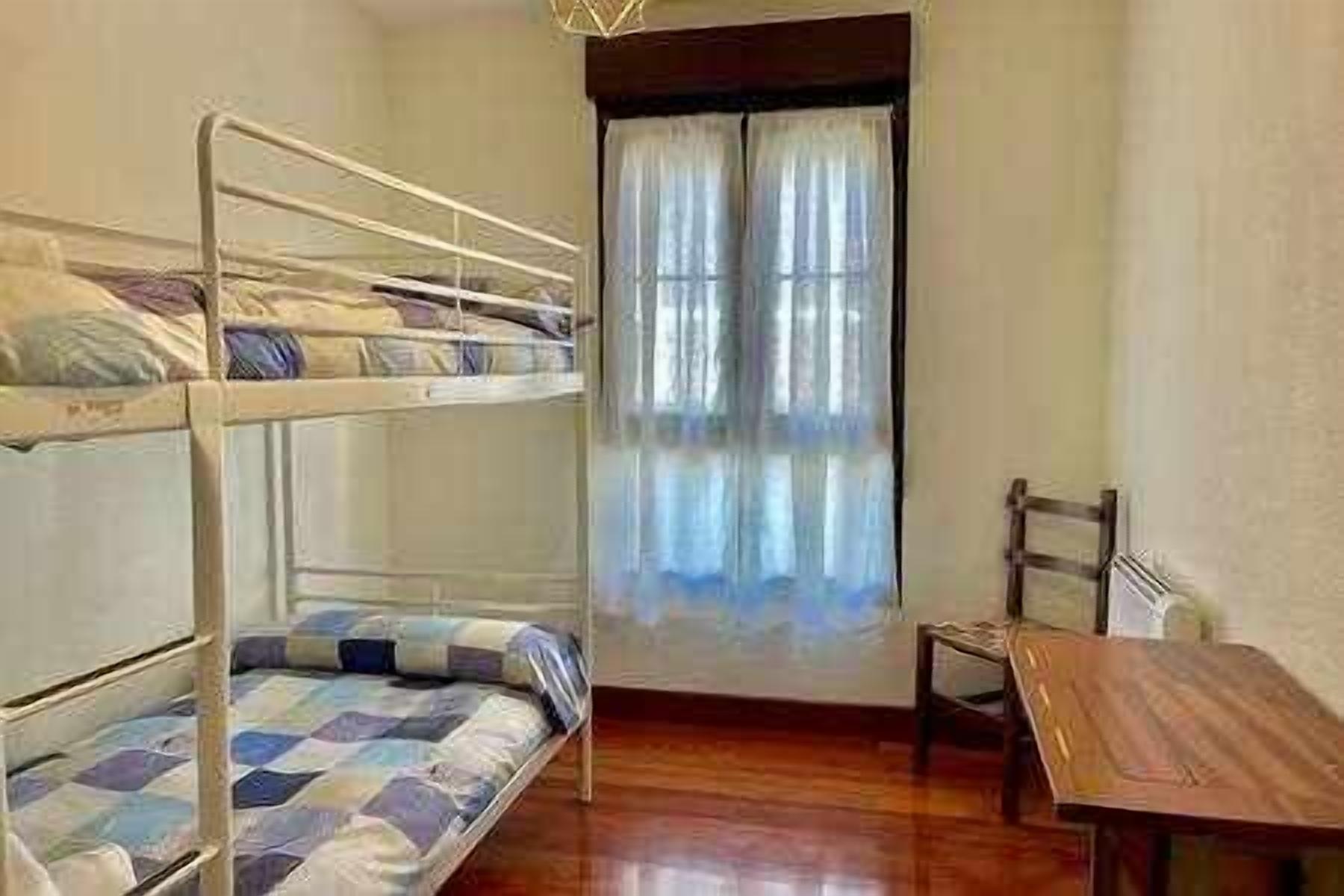 Een kamer met stapelbedden, een houten tafel en een raam met gordijnen.