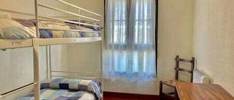 Een kamer met stapelbedden, een houten tafel en een raam met gordijnen.