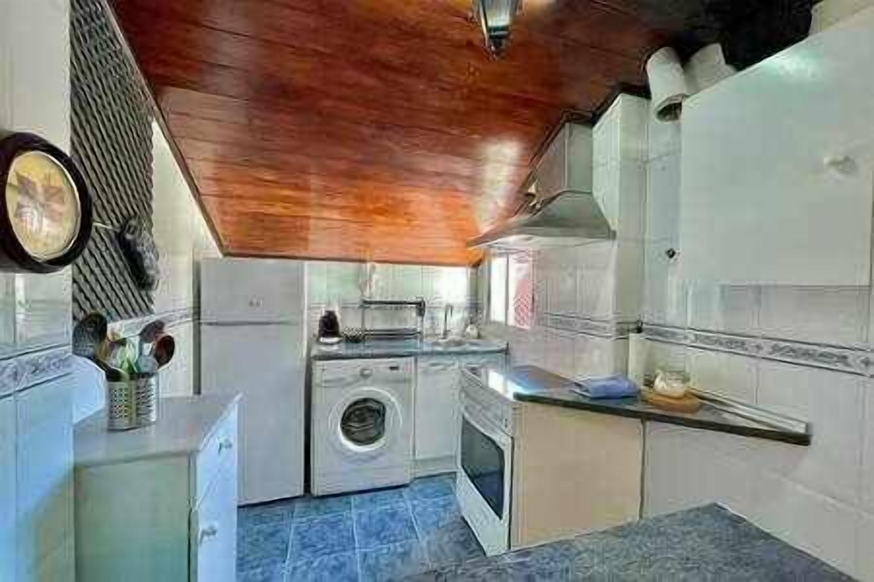Een kleine keuken met een houten plafond, een wasmachine en een kookplaat.