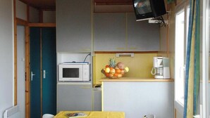 Uma cozinha compacta com micro-ondas, uma fruteira e uma cafeteira.