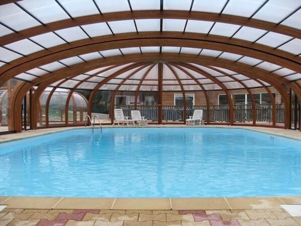 An indoor swimming pool with a wooden arched roof and white lounge chairs.