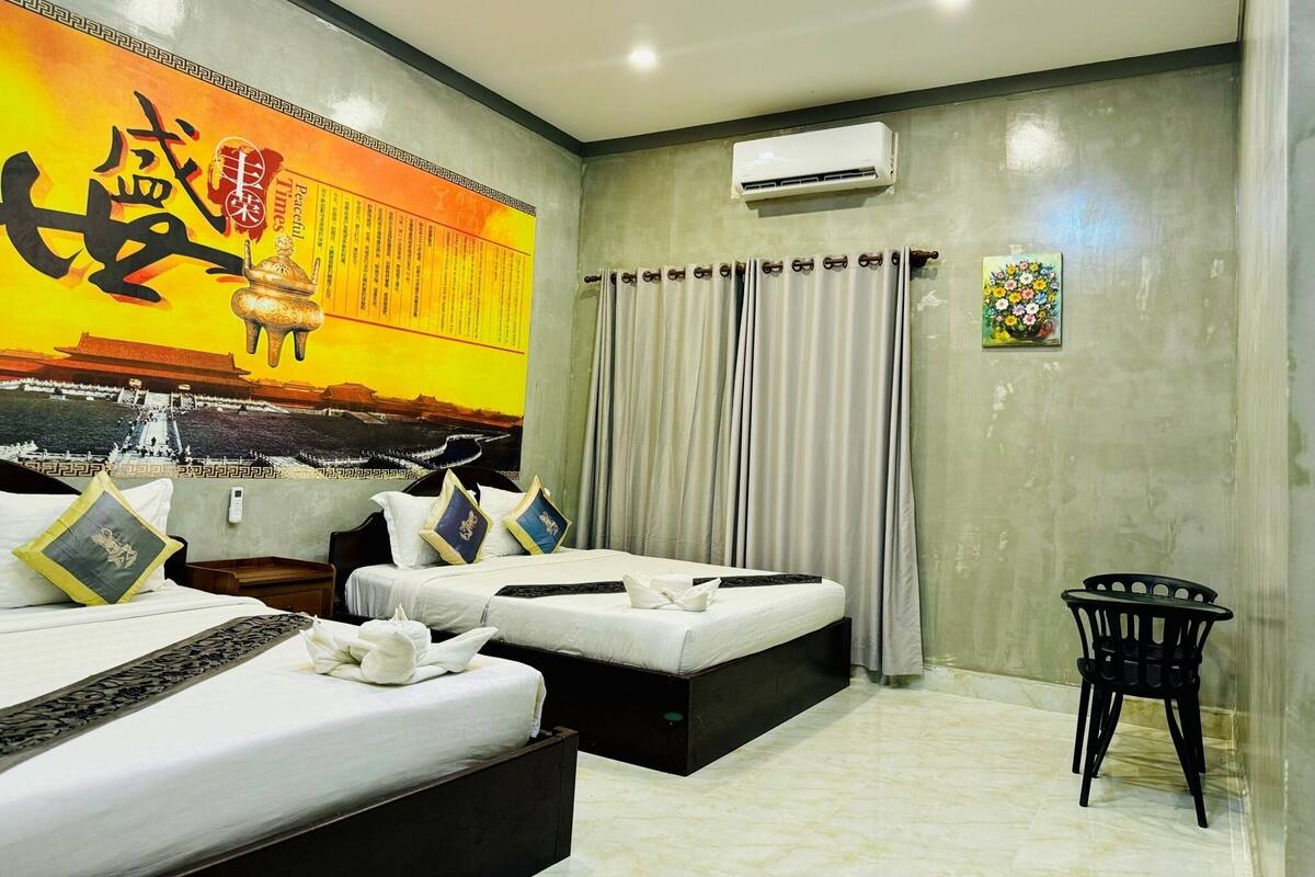 Een hotelkamer met twee bedden, een groot wanddecor, een airconditioning en een klein tafeltje.
