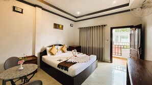 Une chambre d’hôtel avec un lit, un bureau, une chaise, une petite table avec un vase et une porte-fenêtre donnant sur un balcon.